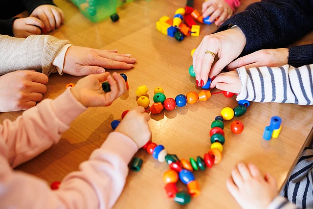 Hände von Kindern und Erzieherinnen, die gemeinsam am Tisch spielen