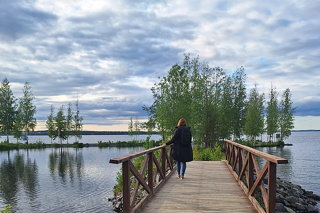 Eine Frau steht auf einer Brücke, vor ihr ein See