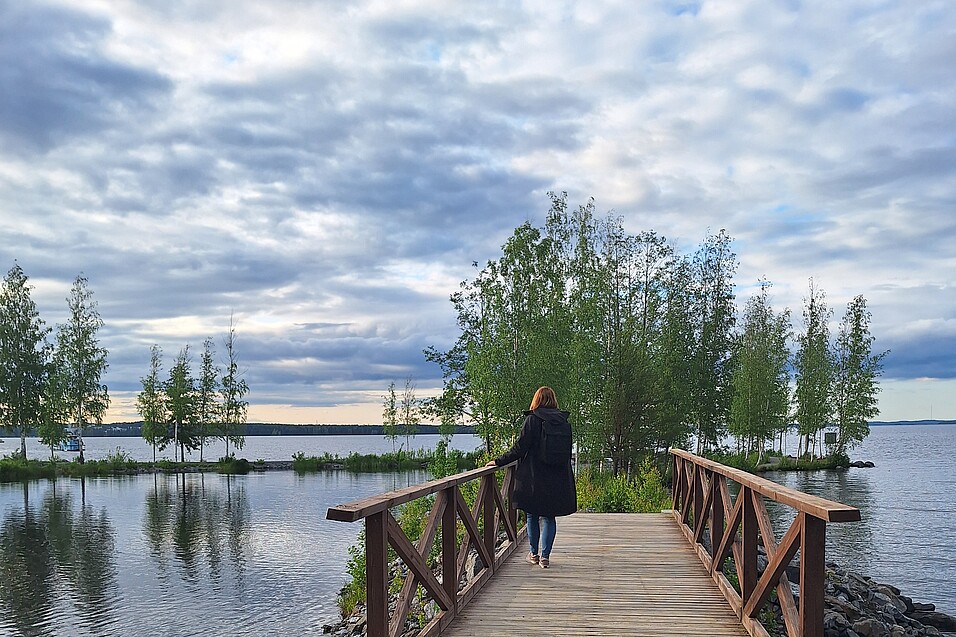 Eine Frau steht auf einer Brücke, vor ihr ein See