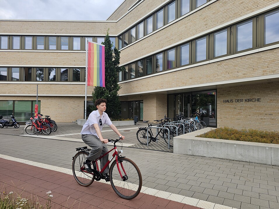 Ein junger Mensch sitzt vor dem Haus der Kirche Niendorf auf einem Fahrrad