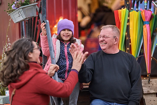 Eine Frau und ein Mann reichen sich die Hand und lachen, ein Kind in der Mitte